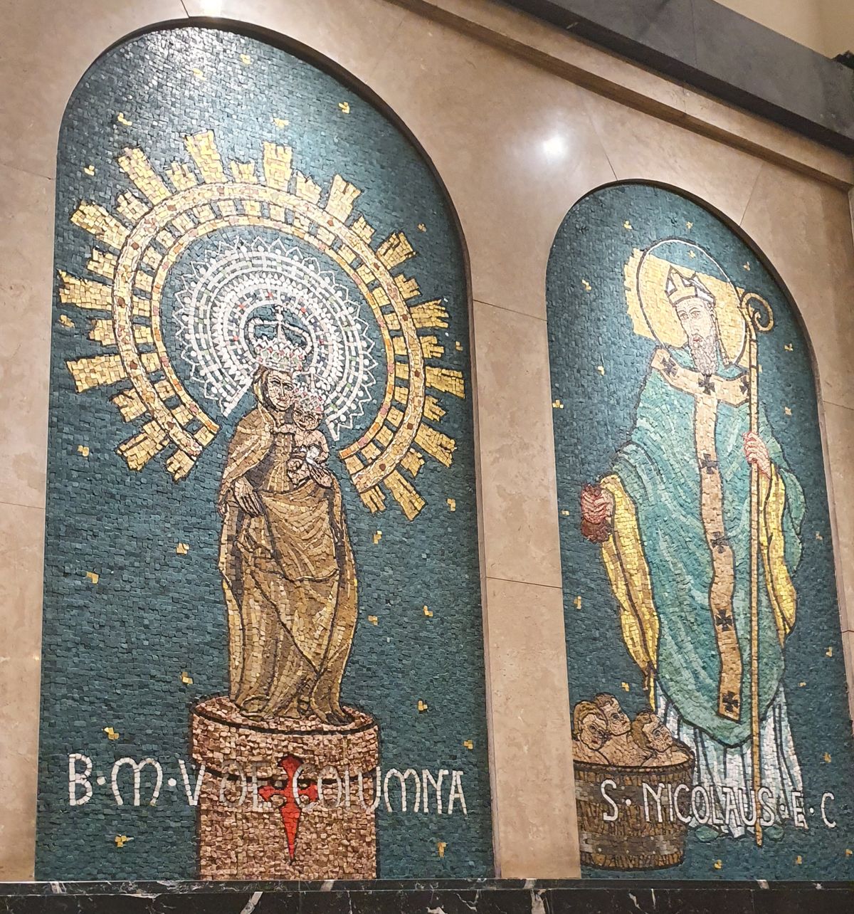 Dos mosaicos de teselas sobre fondo verde con estrellas doradas: la Virgen del Pilar sobre su columna con la cruz de Santiago, y San Nicolás de obispo con báculo y los tres niños en la tina