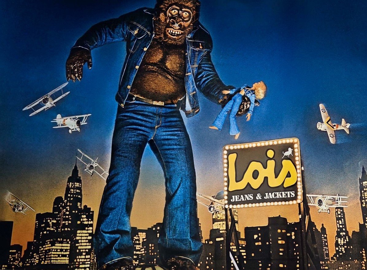 Cartel de publicidad exterior de Lois Jeans & Jackets: un gorila gigante vestido de vaqueros sostiene una muñeca sobre una ciudad nocturna rodeado de biplanos
